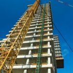 Low-angle view of skyscraper under construction with crane, clear blue sky.